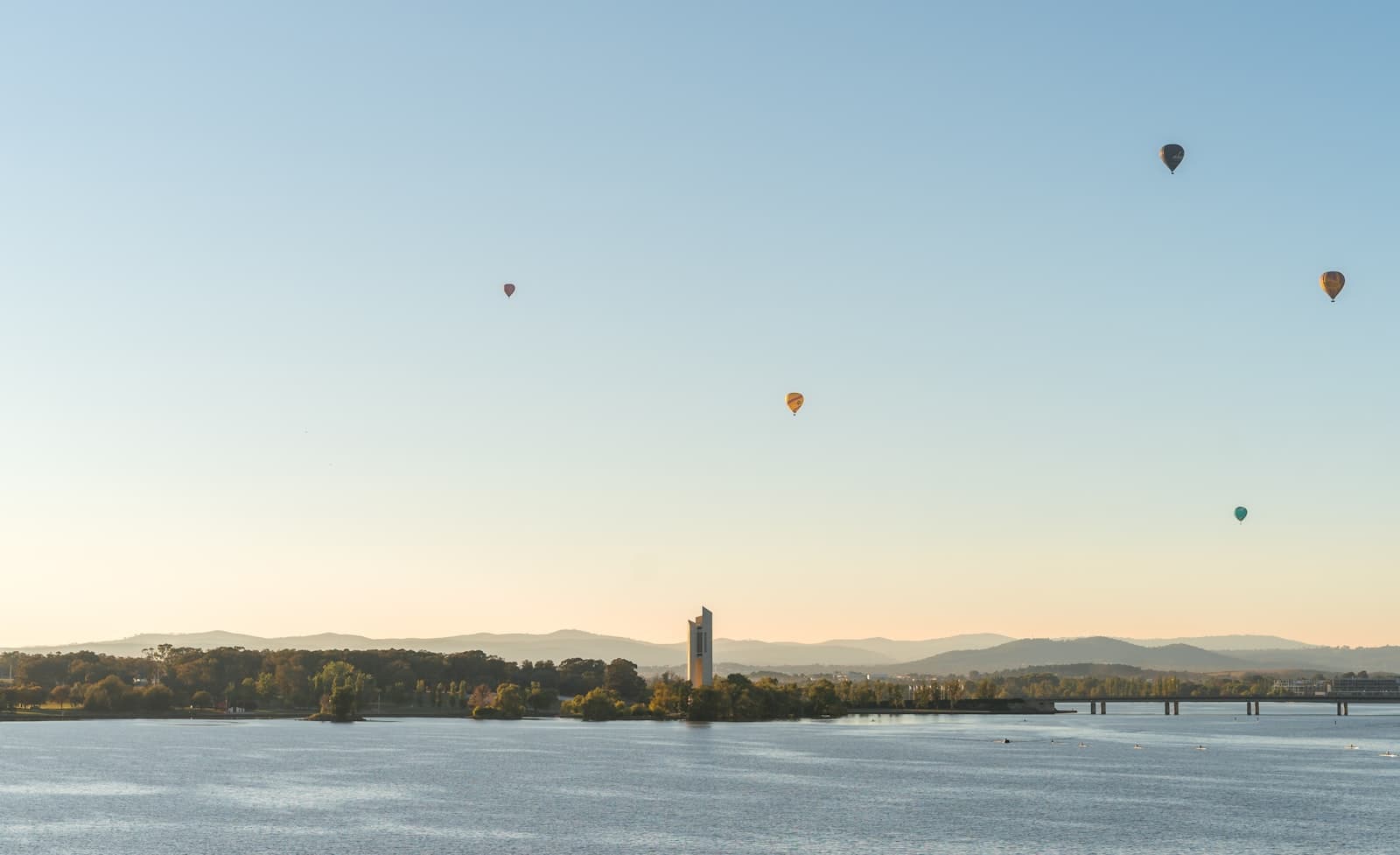 Balloons drifting over Lake Burley Griffin at dawn, the National Carillon below
